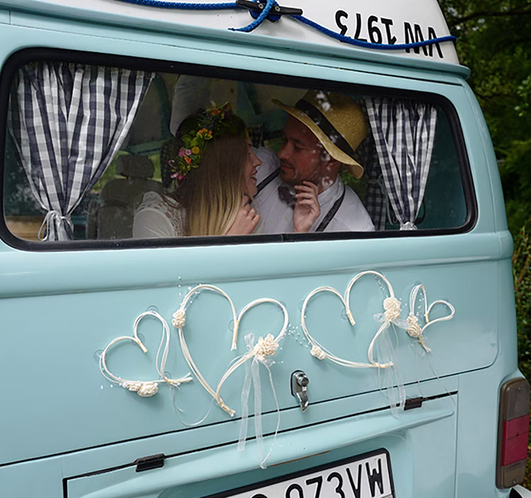 Autoschmuck Hochzeit Herzen Creme 2er Set Rattan Herz mit Saugnapf Hochzeitsaugen Hochzeitswagen Braut & Bräutigam Weding Car geschmücktes Auto Mehrere cremefarbene Rattan-Herzen schmücken die Heckklappe eines Hochzeitsautos, während das Brautpaar im Fahrzeug sitzt.