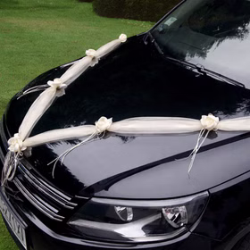 Cremefarbene Organza-Girlande mit Rosenblüten in V-Form auf der Motorhaube eines schwarzen Autos als elegante Hochzeitsdekoration befestigt.