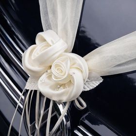 Cremefarbene Organza-Girlande mit Rosenblüten in V-Form auf der Motorhaube eines schwarzen Autos als elegante Hochzeitsdekoration befestigt.