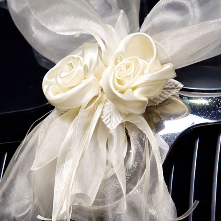 Cremefarbene Organza-Girlande mit Rosenblüten in V-Form auf der Motorhaube eines schwarzen Autos als elegante Hochzeitsdekoration befestigt.