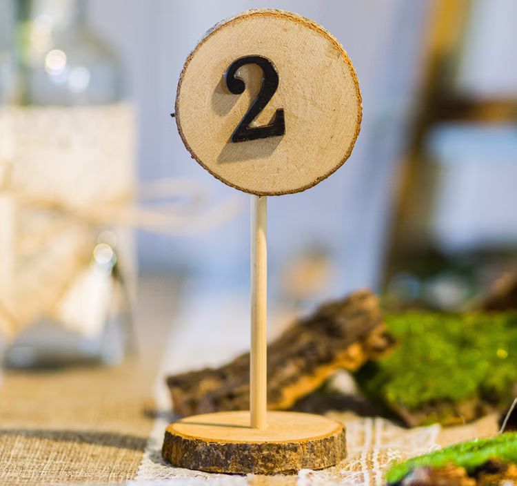 Tisch Nummernhalter Holz 1–10 Hochzeit Geburtstag Baumscheiben Optik SALE Tischdeko gedeckter Tisch Jubiläum Nahaufnahme Tisch Nummernhalter mit der Zahl 2 n natürlicher Baumscheiben-Optik auf einem gedeckten Tisch dekorieret.