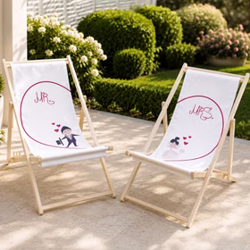 Zwei Hochzeits-Liegestühle mit Mr. und Mrs.-Motiv stehen auf heller Terrasse vor grünem Garten. Hinweis: KI generiertes Bild