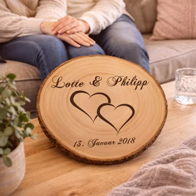 Personalisierte Baumscheibe mit Hochzeitsgravur auf einem Holztisch in einem gemütlichen Wohnzimmer, im Hintergrund sitzt ein Paar auf dem Sofa.