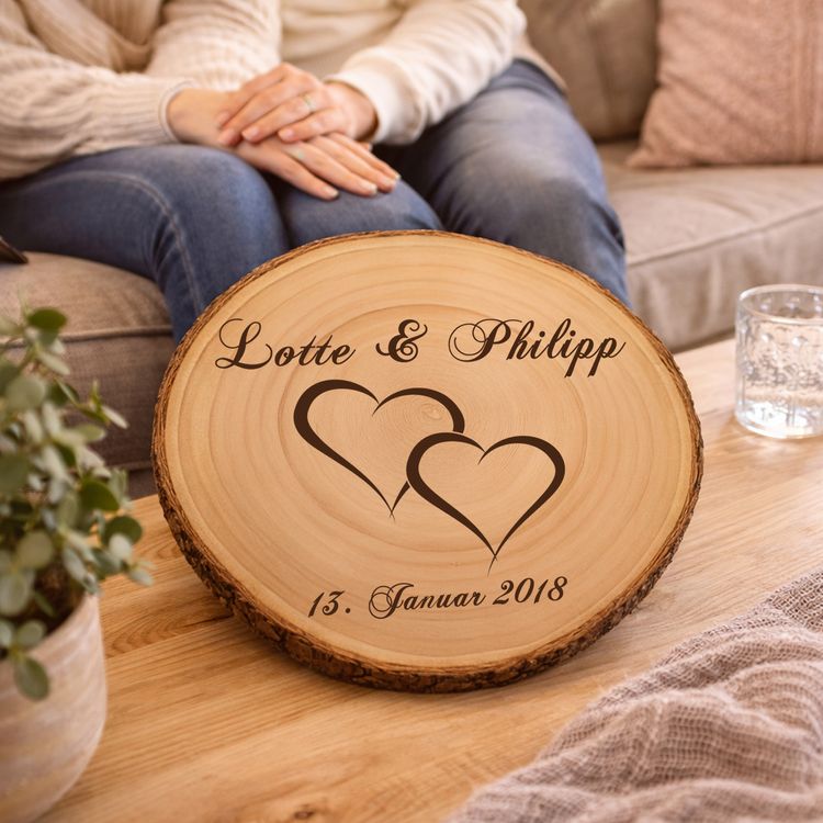 Baumscheibe mit Gravur Doppelherz Namen und Datum Hochzeit Jahrestag Personalisierte Baumscheibe mit Hochzeitsgravur als Dekoration auf einer festlich gedeckten Hochzeitstafel, im Hintergrund ein Brautpaar und Hochzeitsgäste in feierlicher Atmosphäre.