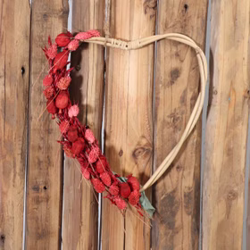 Rattan-Herzen 2er Set Natur 27 & 29 cm Deko-Herzen zum Basteln SALE Hochzeit Dekoration Bastelbedarf Türdeko Geschenk Rattan-Herz hängt an einer Holzwand und ist dekorativ mit roten Trockenblumen geschmückt.