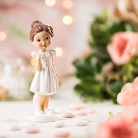 Kommunion Deko Tortenfigur für Kommunionskuchen Mädchen mit Kreuz 15,5 cm weiß Feier Party-Deko Party-Zubehör Erstkommunion Tortenfigur Kommunion Jugendweihe Tisch-Deko Figur Kommunion Mädchen im weißen Kleid mit goldenem Kreuz und brauner Hochsteckfrisur mit Blüte im Haar von Vorne auf gedecktem Tisch.