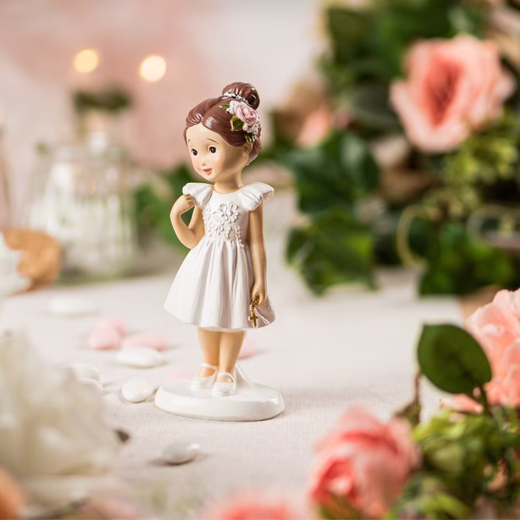 Kommunion Deko Tortenfigur für Kommunionskuchen Mädchen mit Kreuz 15,5 cm weiß Feier Party-Deko Party-Zubehör Erstkommunion Tortenfigur Kommunion Jugendweihe Tisch-Deko Figur Kommunion Mädchen im weißen Kleid mit goldenem Kreuz und brauner Hochsteckfrisur mit Blüte im Haar von der Seite auf gedecktem Tisch.
