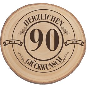 Glückliche ältere Frau mit Familie bei der Geburtstagsfeier, im Vordergrund eine Baumscheibe mit Gravur „Herzlichen Glückwunsch 90“.