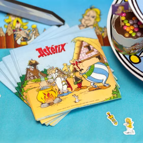 Stapel Asterix-Servietten mit gallischem Dorfmotiv auf türkisfarbener Tischdecke neben Partygeschirr und Dekoration.