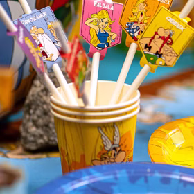 Papierstrohhalme mit Asterix & Obelix Figurenmotiven in Partybecher auf farbenfroher Geburtstagstafel.