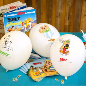 Weiße Luftballons mit Asterix-, Obelix- und Idefix-Motiven dekorativ arrangiert auf einem festlich gedeckten Tisch.