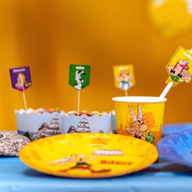 Asterix & Obelix Partybecher mit Comicmotiv auf Geburtstagstisch neben Tellern und Dekoration.