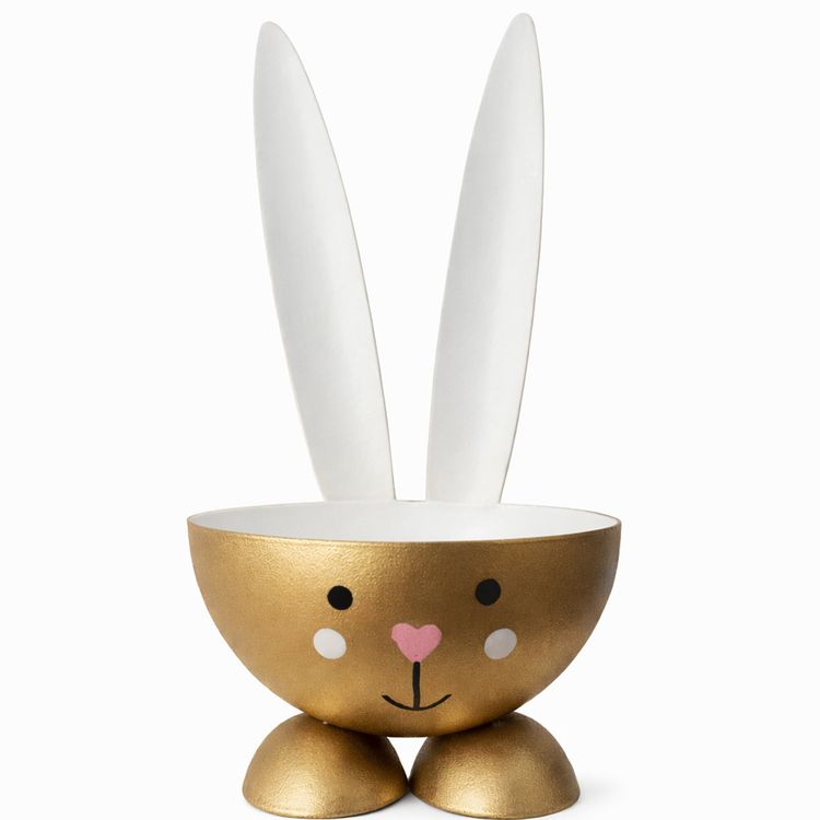 Eierbecher Hase Metall Osterhase 10 cm gedeckter Tisch Ostern Goldfarbener Eierbecher in Form eines Hasen aus Metall mit weißen Ohren, rosa Herz-Nase und kleinen goldenen Füßen auf weißem Hintergrund.