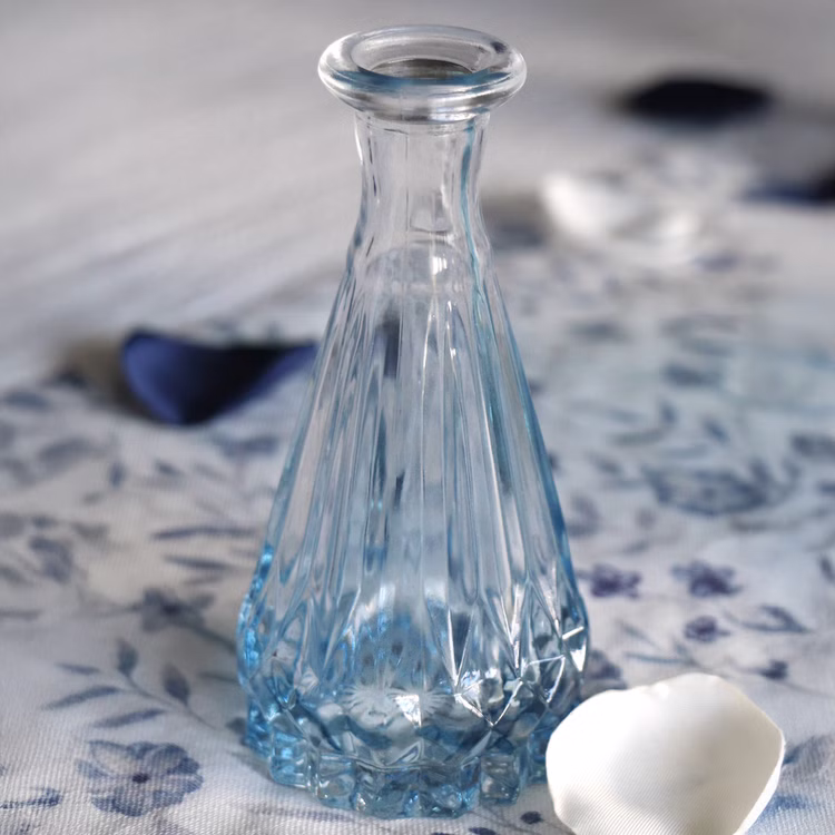 Mini Vase Alexandrin Glasvase 10,7 cm Farbverlauf Blau Tisch-Deko Hochzeit Geburtstag Blumenvase dekorative Vase gedeckter Tisch Kleine blaue Glasvase als Tischdeko, stehend auf blauer Tischdecke mit Rosenblättern.