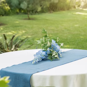 Runder Tisch mit blauem Baumwolle Tischläufer und blauer Blumendeko im Garten.