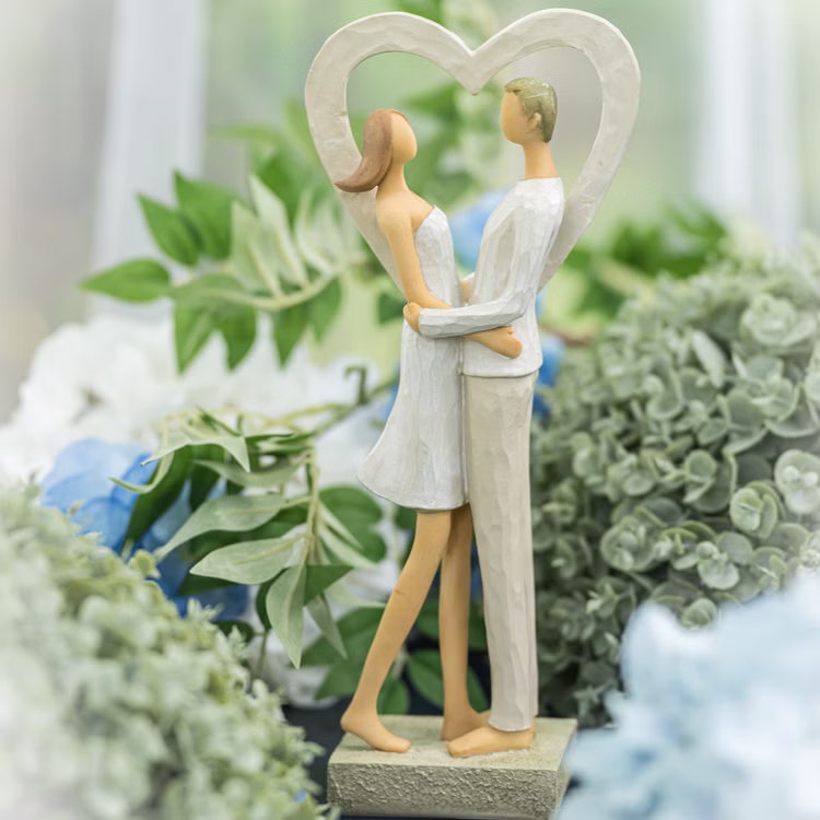 Brautpaar Figur Stehend Liebe Weiß mit Herz Tischdeko Hochzeits-Deko Tisch-Deko Deko-Ideen Geschenkidee Braut & Bräutigam Figur eines Paares im Herzrahmen, aufgestellt zwischen grüner und blauer Blumendeko.