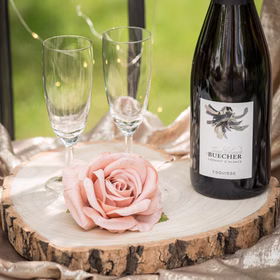 Dekorierte Holzscheibe mit Sektflasche, Gläsern und rosa Rose.