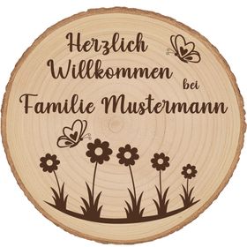 Personalisierte Baumscheibe mit Rinde und Gravur „Herzlich Willkommen bei Familie Schmidt“, dekoriert mit Schmetterlingen und Blumenmotiv, platziert in einem farbenfrohen Sommer-Blumenbeet am Hauseingang.