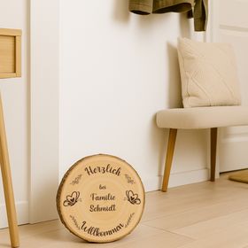 Personalisierte Baumscheibe als Willkommensschild im sommerlichen Blumenbeet vor einem Hauseingang, mit Gravur und Schmetterlingsmotiv.