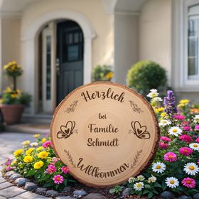 Personalisierte Baumscheibe als Willkommensschild im sommerlichen Blumenbeet vor einem Hauseingang, mit Gravur und Schmetterlingsmotiv.
