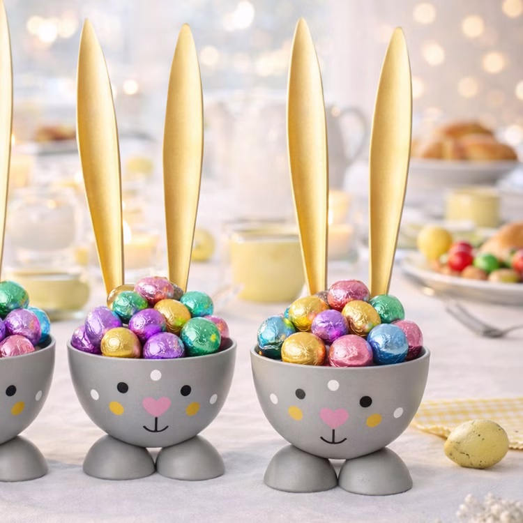2 Eierbecher Hase Grau aus Metall Osterhase 10 cm gedeckter Tisch Ostern Oster-Deko Dekoration Frühling Osterfest Osterbrunch Tisch-Deko Graue Hasen-Eierbecher mit langen goldenen Ohren, gefüllt mit bunten Schokoladeneiern in glänzender Folie, auf einem hell dekorierten Osterbrunch-Tisch.