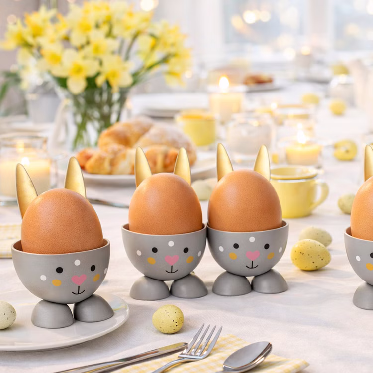 Eierbecher-Set Gold & Grau Hase Bunny 6 Stück Osterhasen-Brunch Tisch-Deko Oster-Deko Dekoration Frühling Osterfest Osterbrunch Tisch-Deko Mehrere graue Hasen-Eierbecher mit goldenen Ohren und braunen Hühnereiern auf einem hell gedeckten Oster-Frühstückstisch mit Blumen, Kerzen und Gebäck im Hintergrund.