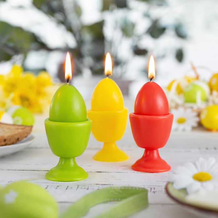 Drei bunte Kerzen in Eierform mit integriertem Eierbecher-Design in Rot, Grün und Gelb vor weißem Hintergrund.