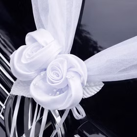Nahaufnahme einer weißen Organza-Girlande mit zwei dekorativen Rosenblüten auf der Motorhaube eines schwarzen Autos befestigt.
