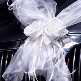 Große weiße Rosenblüten mit Organza-Schleifen als Autoschmuck auf einem Kühlergrill befestigt.