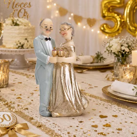 Dekorative Tischszene zur goldenen Hochzeit mit Tortenaufsatz eines älteren Ehepaares, goldenen Accessoires, Kerzen und festlicher Dekoration.