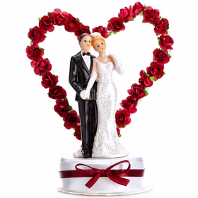 Tortenaufsatz Hochzeitspaar mit rotem Rosenherz, Braut in weißem Kleid und Bräutigam im schwarzen Anzug auf Sockel mit roter Schleife.