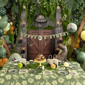 Komplett dekorierter Jurassic World Geburtstagstisch mit Banner, Ballons, Geschirr, Tüten und Dino-Kulisse.