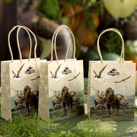 Drei Jurassic World Geschenktüten auf dekoriertem Partytisch mit grüner Dino-Deko im Hintergrund.