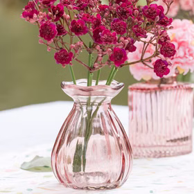 Kleine rosafarbene Glasvase mit pinken Blüten als stilvolle Tischdekoration – detailreiche Mini-Vase aus Glas.
