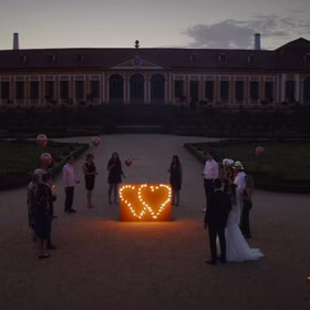 Lichterbild Brennendes Doppelherz mit Brautpaar und Hochzeitsgästen in der Abenddämmerung.