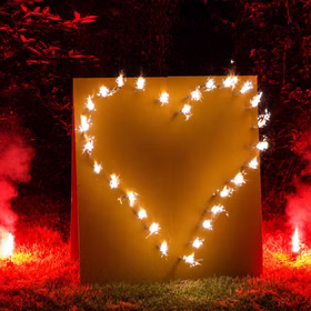 Nahaufnahme Lichterbild Brennendes Herz mit Bengalfeuer auf einer Wiese vor dunklem Hintergrund.