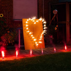 Brennendes Herz-Lichterbild mit Bengalfeuern auf einer Terrasse vor einem Haus bei Nacht.